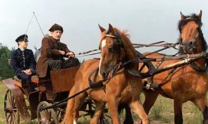 Dwóch mężczyzn w strojach z epoki jedzie w bryczce zaprzężonej w dwa konie.