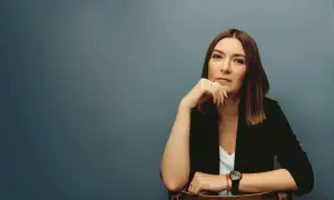 Kobieta w czarnej marynarce siedzi, opierając podbródek na dłoni.