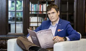 Mężczyzna w niebieskiej marynarce siedzi w fotelu i czyta czasopismo "Academia".