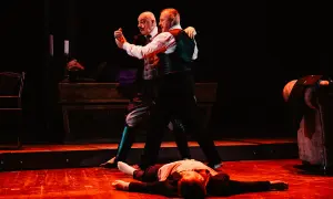 Dwóch mężczyzn tańczy tango, trzeci leży na podłodze.