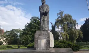 Pomnik Adama Mickiewicza na tle błękitnego nieba i zieleni.