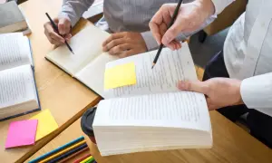 Dwie osoby uczące się przy biurku, otwarte książki, notatki i kredki.