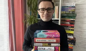 Mężczyzna w czarnym golfie trzyma stos kolorowych książek.