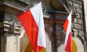 Dwie polskie flagi powiewają na tle zabytkowej kamienicy.