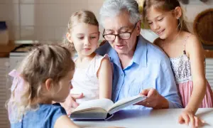 Babcia czyta książkę trzem wnuczkom przy stole.