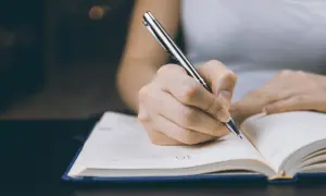 Dłoń pisząca długopisem w otwartym notatniku.