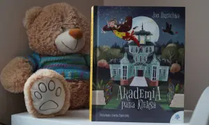 Pluszowy miś obok książki "Akademia Pana Kleksa" z ilustracją latającego Ambrożego Kleksa.