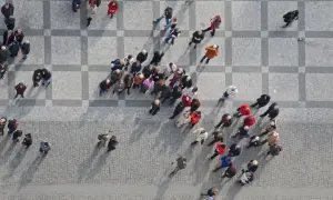 Widok z góry na grupę ludzi spacerujących po brukowanym placu z geometrycznym wzorem.