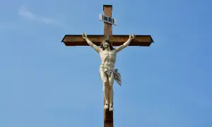 Figurka Jezusa na drewnianym krzyżu z tabliczką INRI na tle błękitnego nieba.