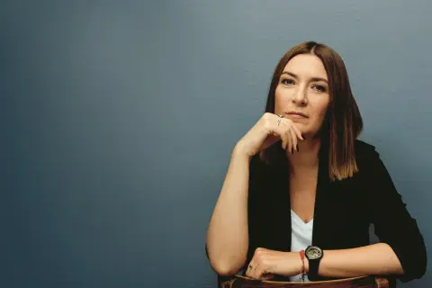 Kobieta w czarnej marynarce siedzi, opierając podbródek na dłoni.