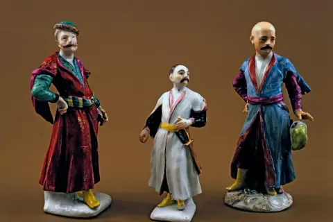 Trzy porcelanowe figurki szlachciców w strojach sarmackich.