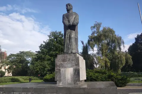 Pomnik Adama Mickiewicza na tle błękitnego nieba i zieleni.