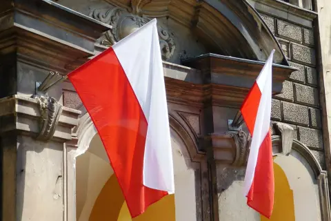 Dwie polskie flagi powiewają na tle zabytkowej kamienicy.