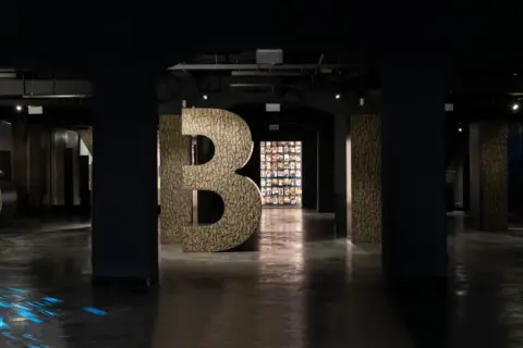 Wielkie litery "S", "Y", "B", "I", "R" w ciemnym wnętrzu, z niebieskimi refleksami na podłodze.