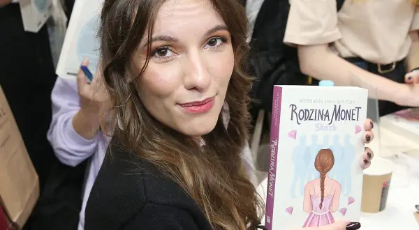 Kobieta trzyma książkę "Rodzina Monet. Skarb" z ilustracją dziewczynki i sylwetek rodziny.