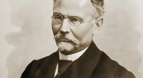 Portret mężczyzny w okularach i z wąsami, ubranego w garnitur.