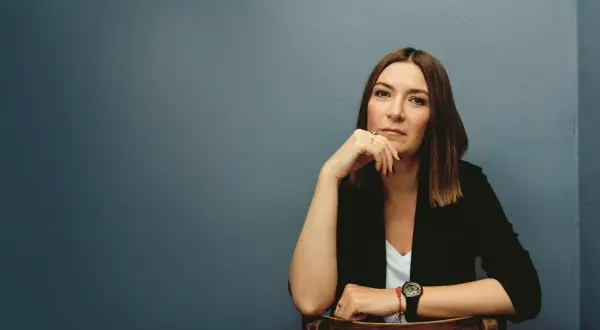 Kobieta w czarnej marynarce siedzi, opierając podbródek na dłoni.