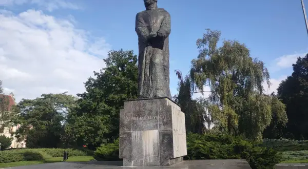 Pomnik Adama Mickiewicza na tle błękitnego nieba i zieleni.
