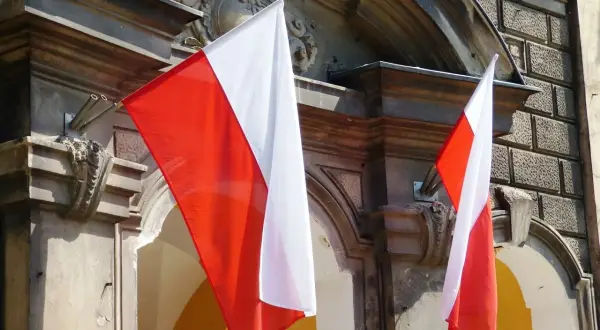 Dwie polskie flagi powiewają na tle zabytkowej kamienicy.
