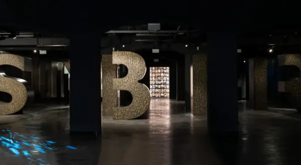 Wielkie litery "S", "Y", "B", "I", "R" w ciemnym wnętrzu, z niebieskimi refleksami na podłodze.