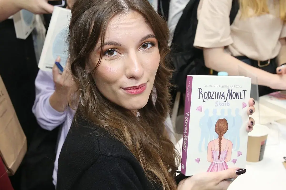 Kobieta trzyma książkę "Rodzina Monet. Skarb" z ilustracją dziewczynki i sylwetek rodziny.