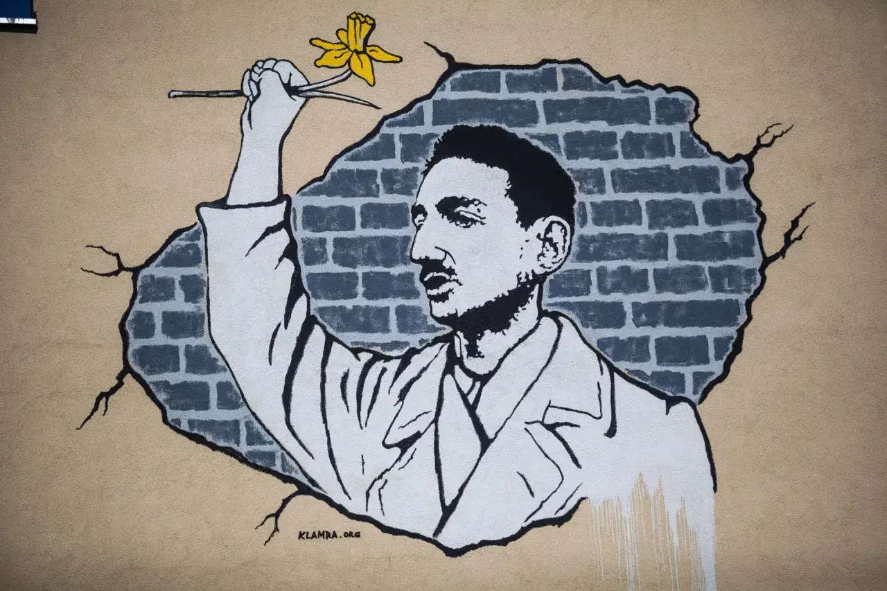 Mural przedstawiający mężczyznę z żółtym żonkilem na tle zniszczonej ceglanej ściany.