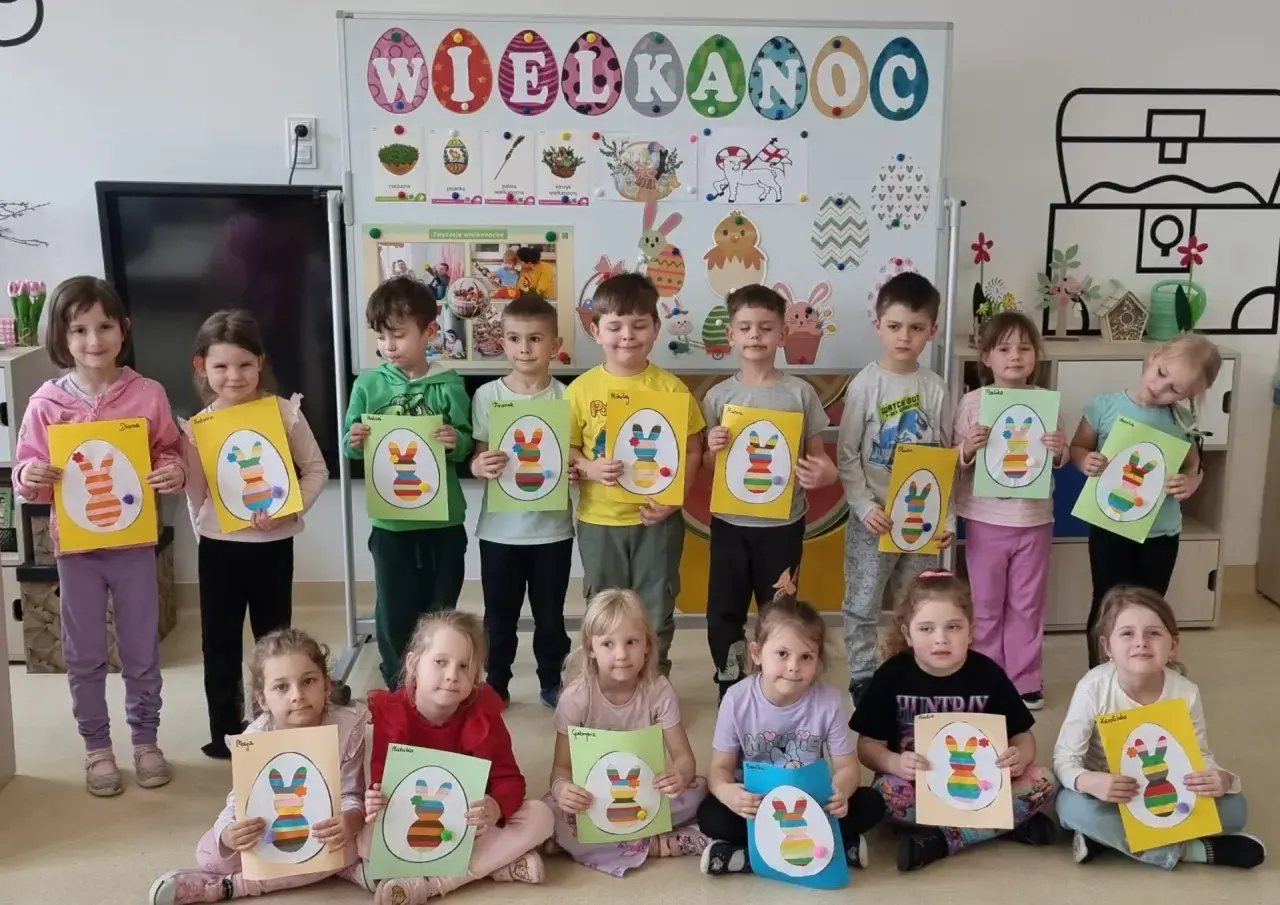 Dzieci trzymające prace plastyczne z wielkanocnymi króliczkami.
