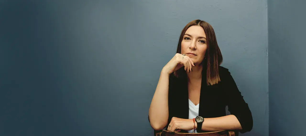 Kobieta w czarnej marynarce siedzi, opierając podbródek na dłoni.