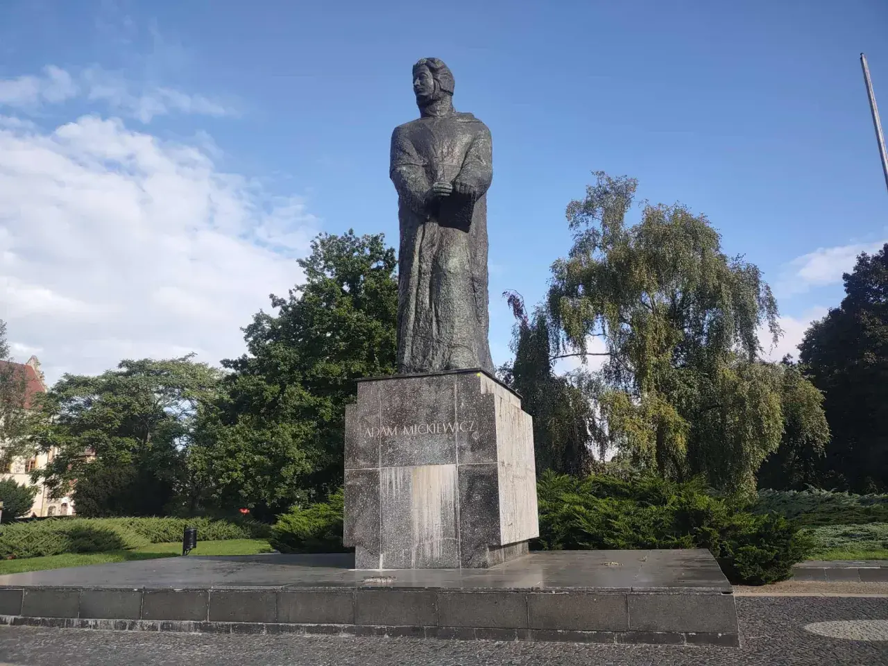 Pomnik Adama Mickiewicza na tle błękitnego nieba i zieleni.