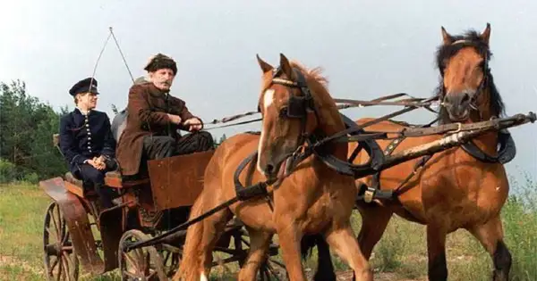 Dwóch mężczyzn w strojach z epoki jedzie w bryczce zaprzężonej w dwa konie.