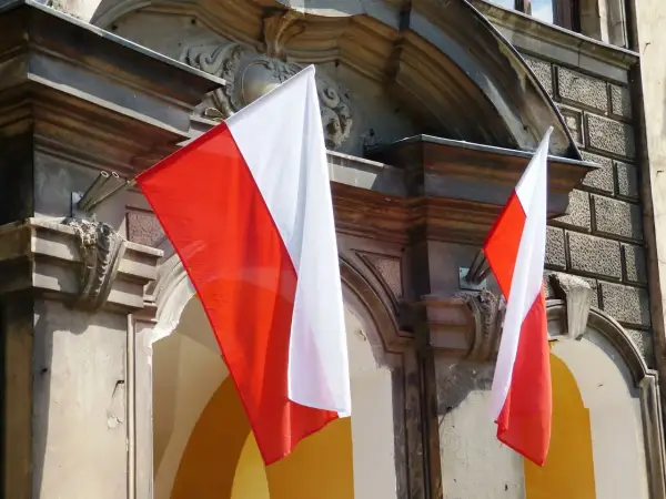 Dwie polskie flagi powiewają na tle zabytkowej kamienicy.
