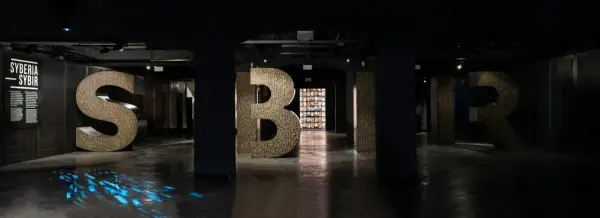 Wielkie litery "S", "Y", "B", "I", "R" w ciemnym wnętrzu, z niebieskimi refleksami na podłodze.