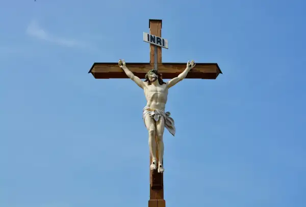Figurka Jezusa na drewnianym krzyżu z tabliczką INRI na tle błękitnego nieba.